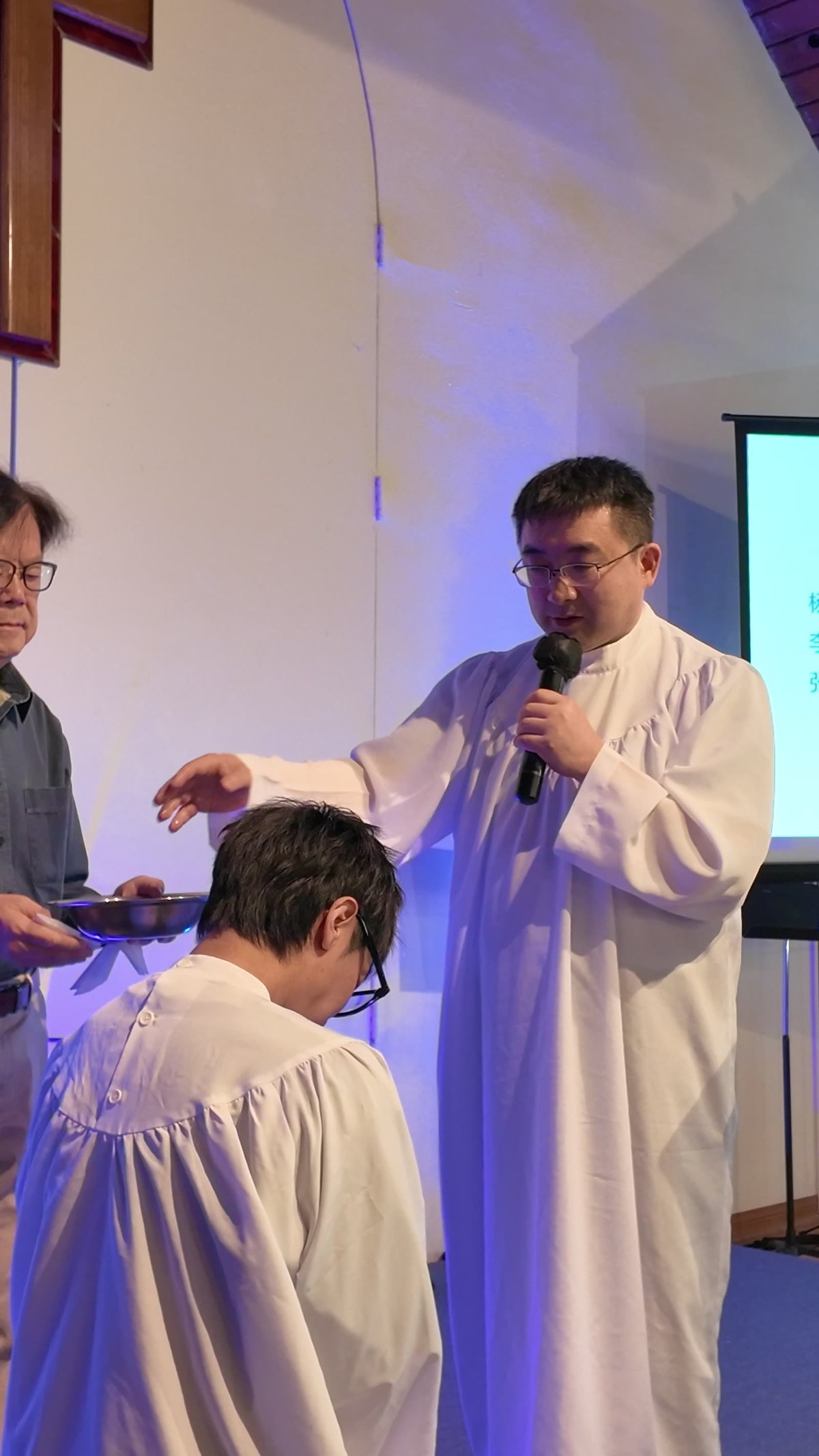 牧师穿着白袍，按手为低头的受洗者施洗