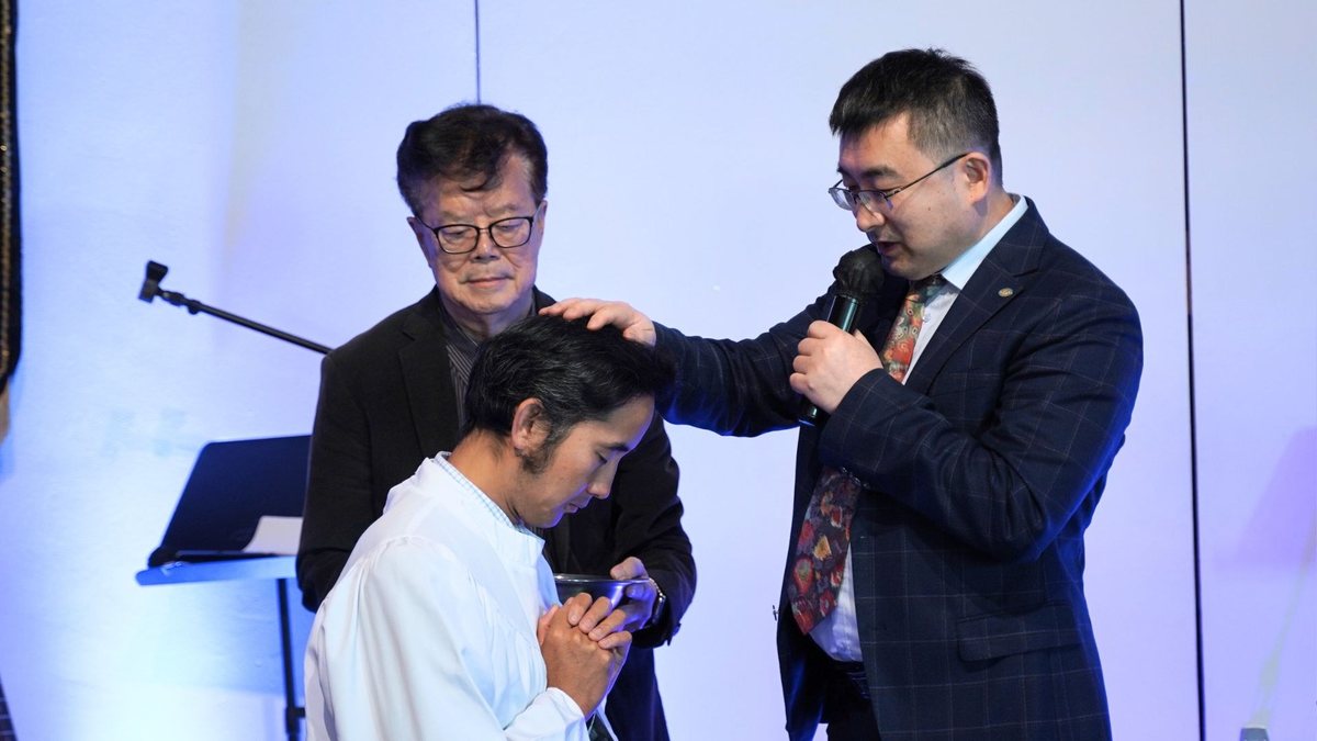 受洗者双手合十低着头，牧师在一旁为他祷告