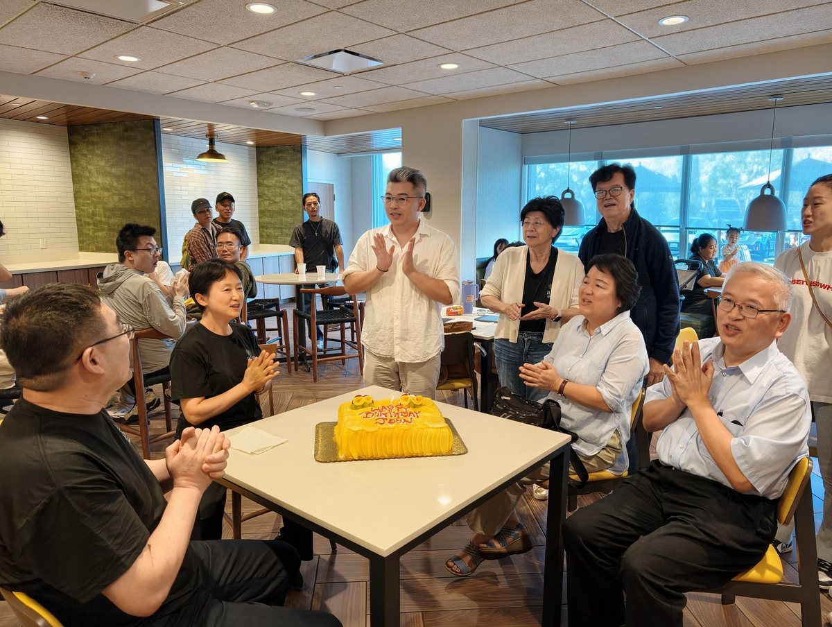 大家围着桌上的生日蛋糕鼓掌，长辈坐在一旁
