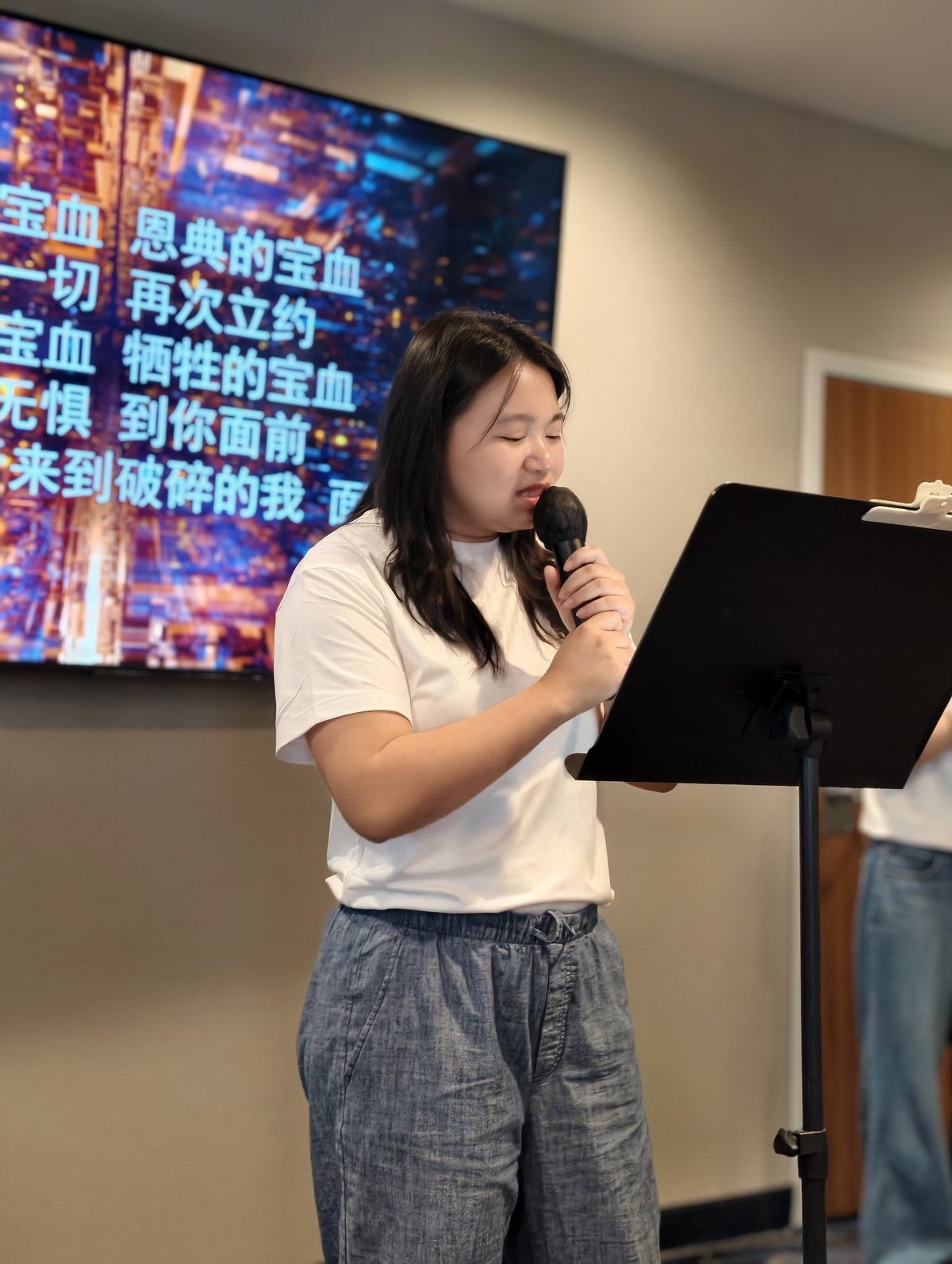 姊妹拿着麦克风唱诗，身后的屏幕打着歌词
